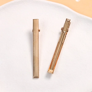 Detail view of two gold-plated metal duckbill hair clips with a smooth polished finish
