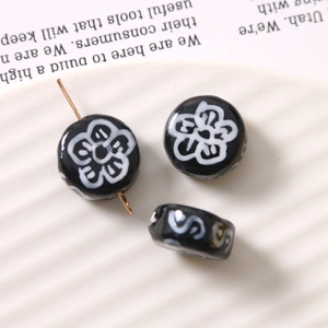Macro detail of black glass beads with white plum blossoms and side holes for DIY jewelry