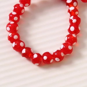 Détail macro de perles en verre rouge 10mm à pois blancs pour la création de bijoux