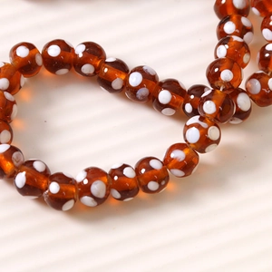Vue macro de perles en verre ambré de 10mm avec pois blancs pour création de bijoux