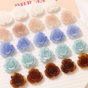Matte resin rose charms in multiple colors on a textured white tray for DIY jewelry