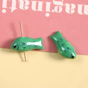 Makroaufnahme grüner Koi-Fischperlen aus Keramik mit goldenem Metallstift für DIY-Schmuck