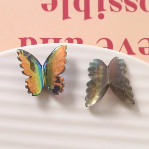 Dettaglio di ciondoli a farfalla in resina AB iridescente su vassoio in ceramica bianco