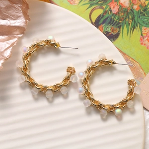 Orecchini a C a spirale dorata con perle iridescenti su un vassoio di ceramica
