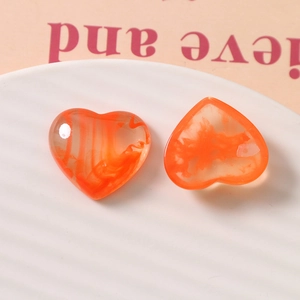 Macro view of orange heart-shaped resin charms with swirl and smoky textures in a tray
