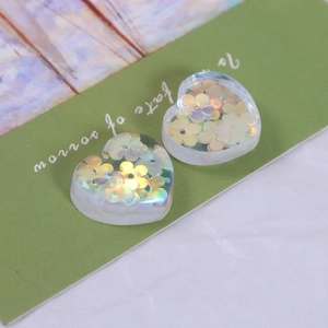 Detail of transparent resin heart charms with iridescent flower sequins for DIY crafts