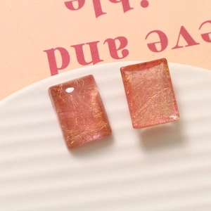 Close-up van roze transparante hars rechthoekige oorbellen met gouden draad textuur