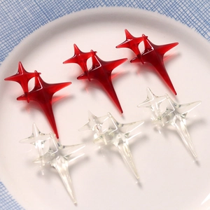 Macro view of transparent and red four-pointed star resin charms on a white plate