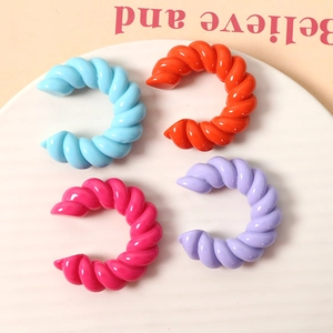 Dettaglio dei polsini auricolari a spirale in resina colorata blu, arancione e rosa