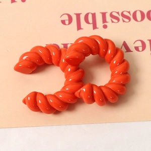 Dettaglio di accessori in resina a doppia C ritorti arancio brillante con trama lucida