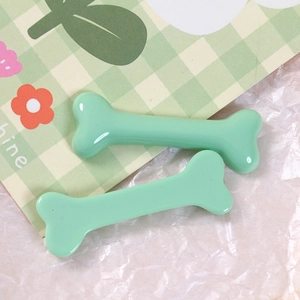 Close-up of mint green bone-shaped resin hair clips with a glossy finish on plaid background