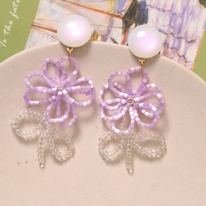 Macro detail of handmade floral earrings with purple matte beads on a ceramic tray