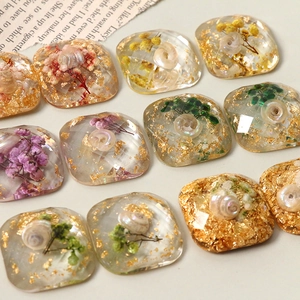 Macro detail of resin charms with dried flowers, gold foil and pearl shells for DIY crafts