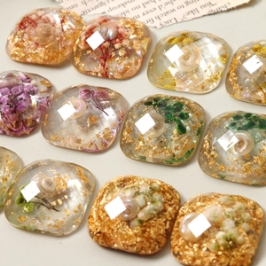 Macro detail of resin charms with gold foil, shells, and dried flowers for DIY jewelry