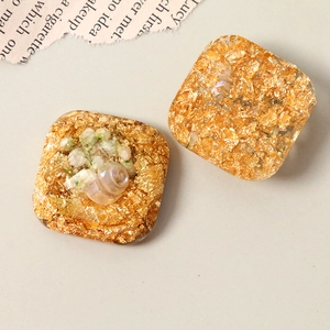 Macro shot of geometric resin earring studs with gold foil, dry flowers and tiny pearls