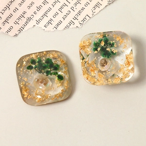Macro detail of geometric resin charms featuring gold foil, shell and mini green beads