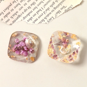 Macro detail of geometric resin charms with purple flowers, shells and gold foil flakes