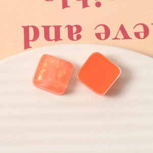 Dettaglio di orecchini quadrati in resina arancione da 15mm con glitter dorati su vassoio