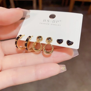 Detailliertes Set aus schwarzen Herzohrsteckern und goldenen Creolen in der Hand
