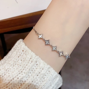 Elegant silver star bracelet with white shell inlays worn on wrist with knit sweater