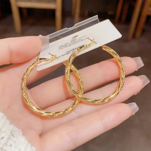 Makro-Detail von großen goldenen gedrehten Creolen mit feiner Textur auf weißer Karte