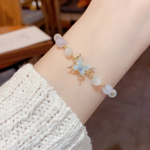 Elegant beaded bracelet with cat eye stones and a blue butterfly charm on a woman's wrist