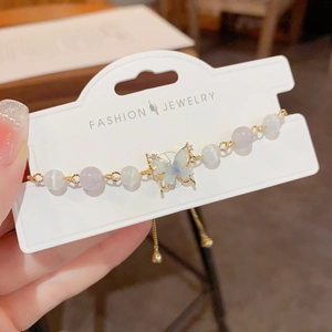 Adjustable gold bracelet with blue butterfly pendant, cat eye beads, and silk tassel charm