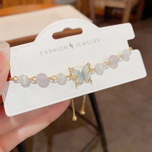 Detail of beaded bracelet showing cat-eye stone beads and a gold butterfly pendant with crystals