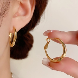 Gros plan de boucles d'oreilles créoles dorées torsadées montrant la texture du métal poli