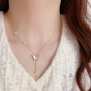 Detail of gold necklace with shell butterfly pendant and pearl tassel on white lace