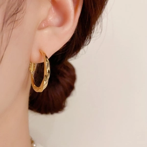 Créoles dorées torsadées minimalistes pour femmes avec finition en métal poli sur l'oreille