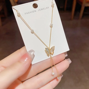 Close-up of golden butterfly pendant necklace with mother-of-pearl wings and pearl tassels