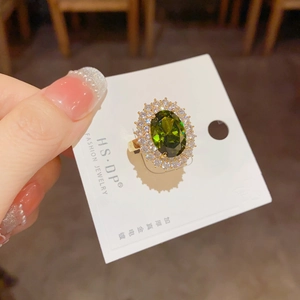 Détail macro d'une bague ouverte dorée avec émeraude ovale et zircons sertis en pavé
