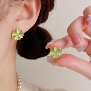 Detail of a rotating light green cat-eye stone clover earring worn on a model ear