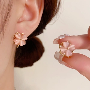 Close-up of pink cat eye stone clover earrings with gold frame on model's ear