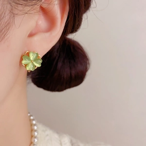 Macro shot of light green clover stud earring with gold edging on ear