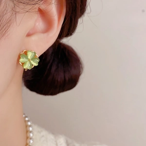 Close-up of elegant four-leaf clover earrings with green stones on a female model