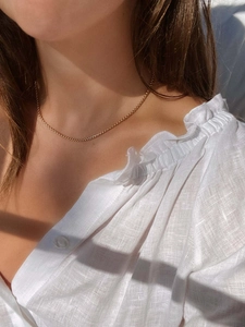Detalle de una cadena de bolas bañada en oro de 18k sobre una camisa de lino