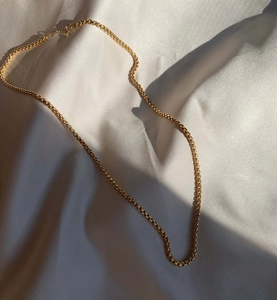 Primer plano de una cadena veneciana chapada en oro de 18k sobre fondo de seda blanca