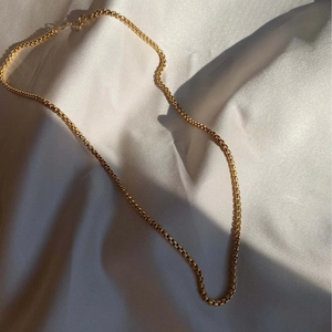 Collar de cadena veneciana chapado en oro de 18k sobre fondo de tela de seda blanca pura