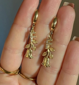 Detail von goldenen Creolen mit einem diamantbesetzten F und Rosenblüten-Anhänger