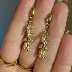Goldene T-Bügel Ohrringe mit F-Buchstaben und Rosenanhänger an der Hand