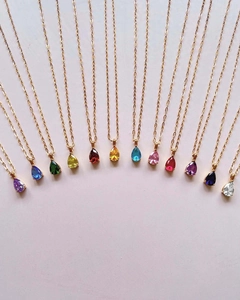 Detailed overhead view of twelve colorful teardrop crystal necklaces with 18k gold chains