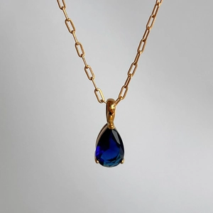 Detail view of pear-shaped blue sapphire pendant on a gold paperclip link chain necklace