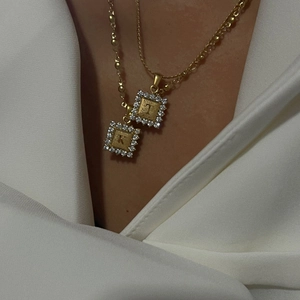 Detail van 18k vergulde gelaagde kettingen met vierkante letterhangers bezet met diamanten