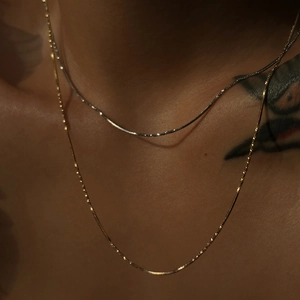 Close-up of gold and silver snake chain necklaces layered on a woman's collarbone