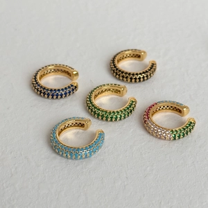Σετ χρυσά σκουλαρίκια ear cuff με πολύχρωμα ζιργκόν σε λευκή ανάγλυφη επιφάνεια