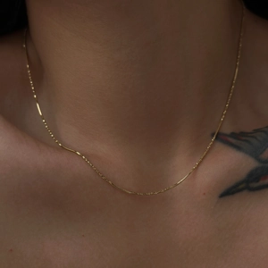 Detailed close-up of 18k gold plated herringbone snake chain on a female collarbone