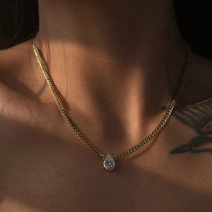 Close-up of 18k gold plated pear-shaped zircon pendant on a textured chain worn by a model