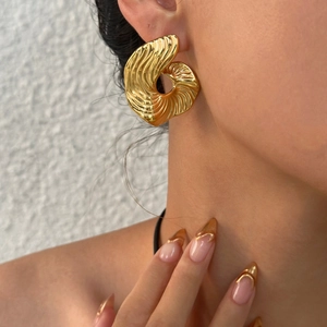 Détail macro de boucles d'oreilles éventail dorées avec structure ondulée et fini poli